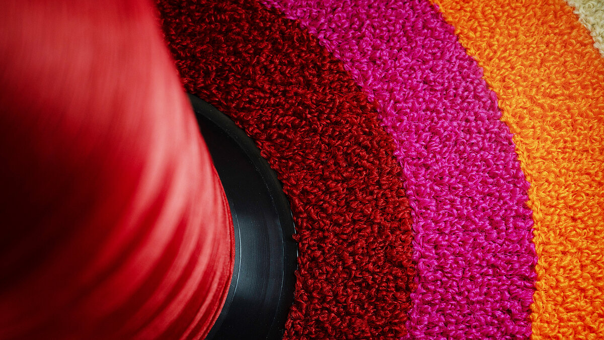Eine rote Chenille-Kone, eingebettet in einen farbenfrohen, mit Chenille bestickten Kreis in Rot-, Rosa- und Orangetönen.